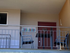 Un balcón con barandillas de metal, una puerta roja y un adorno en la pared.