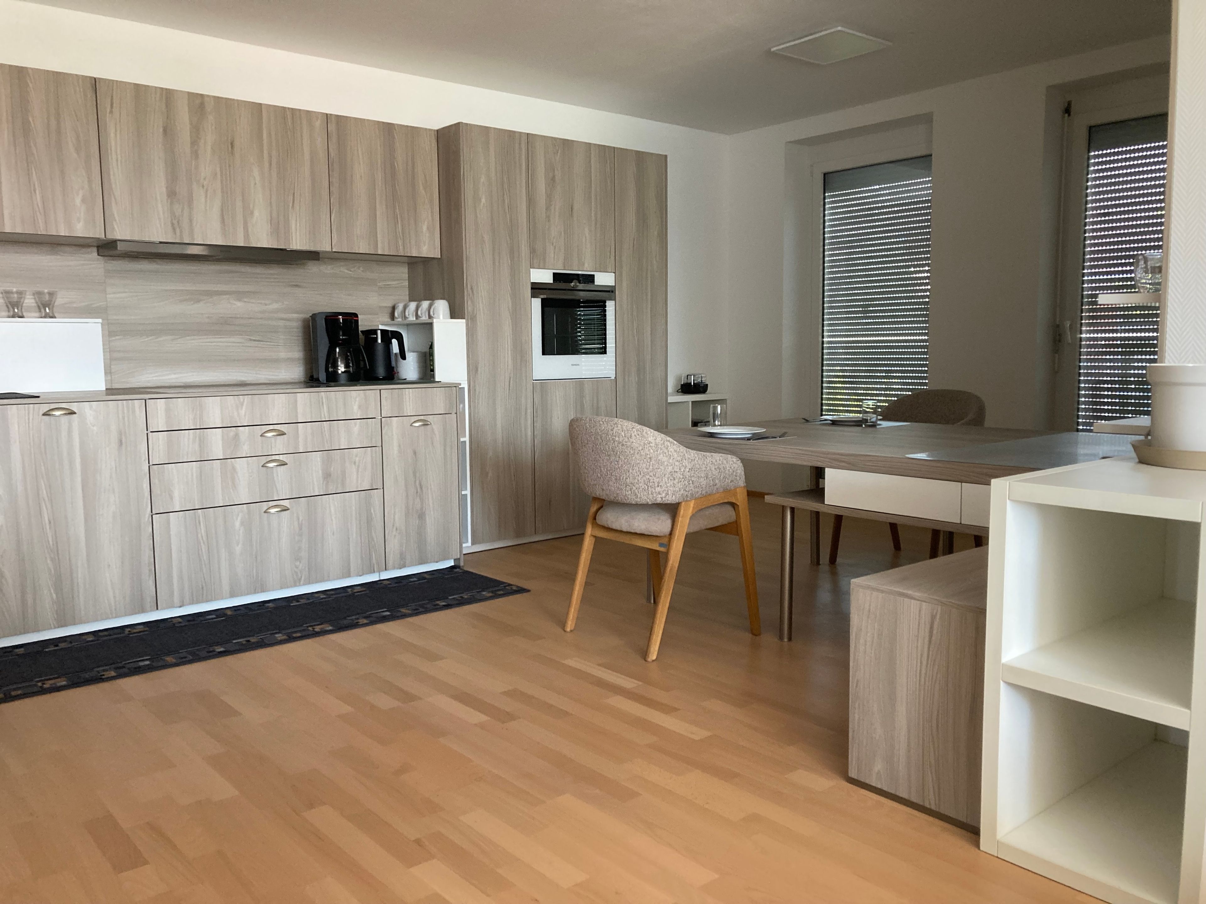 Een moderne keuken met houten kastjes, een eethoek met een stoel en een inbouwoven.