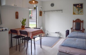 Ein Zimmer mit Esstisch, Stühlen, einem Bett, einem Heizkörper, einer Uhr und einem Gemälde.