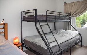 Ein Etagenbett mit einer Leiter, ein Nachttisch mit Lampe und ein Fenster mit Vorhängen.