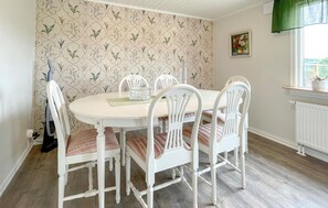 Un coin repas avec une table ronde, des chaises blanches, un papier peint à motifs floraux et une fenêtre donnant sur un beau paysage.