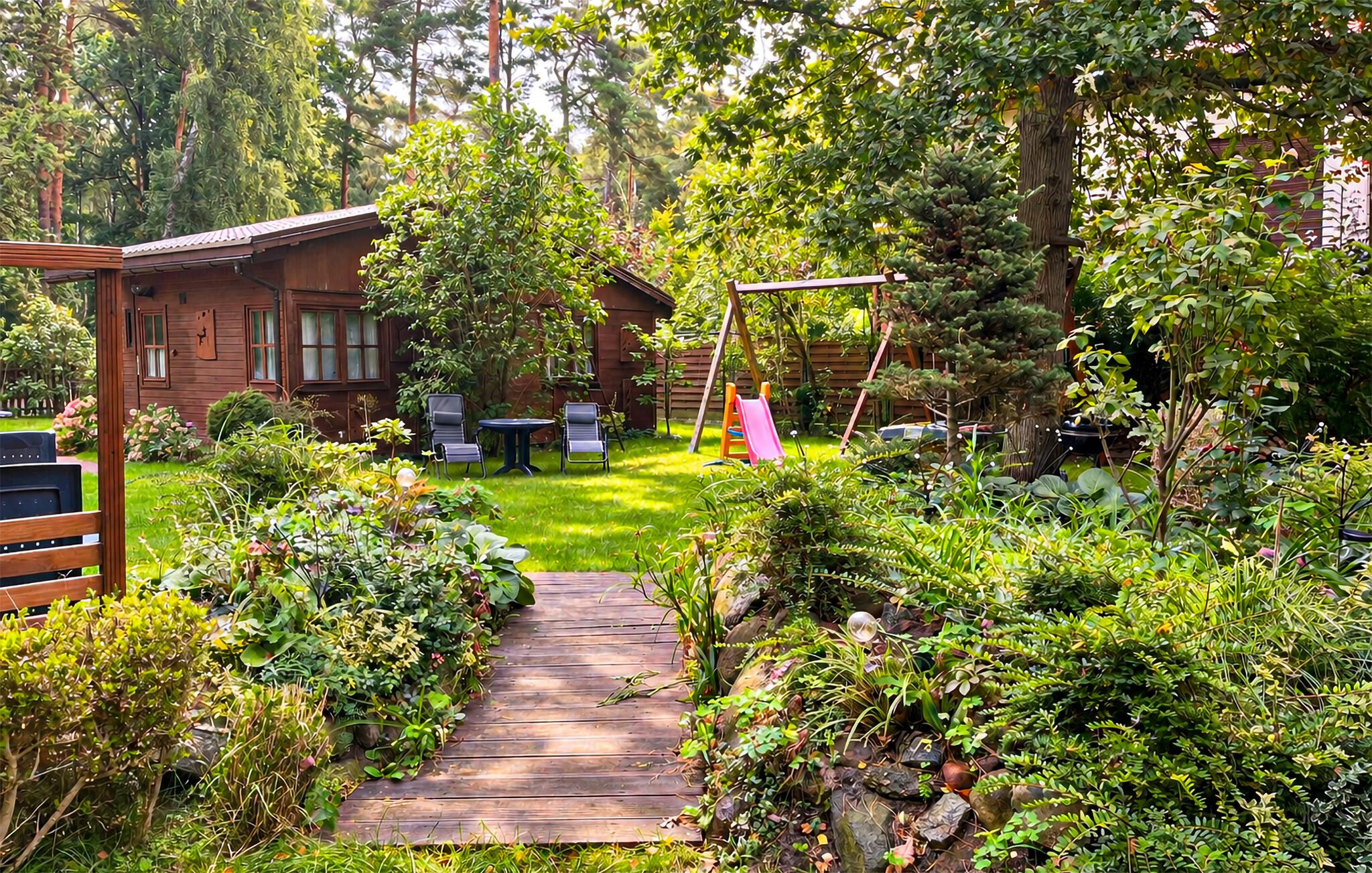 A wooden deck leading to a house with a swing set and a small table with chairs.