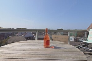 A wooden table with a bottle on it, a glass chair, and a view of houses and hills in the background. - Residence de l'Europe / Noordstraat 19D (Domburg)