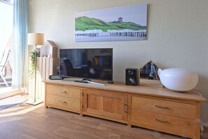 A modern living room with a flat-screen TV, wooden cabinet, and a painting of a coastal landscape. - Residence de l'Europe / Noordstraat 19D (Domburg)