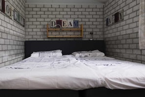 Une pièce avec un mur en briques, un lit avec une literie blanche et une étagère sur laquelle est écrit le mot « RÊVE ».