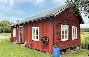 Punainen puutalo, jossa on metallikatto, polkupyörä ja sininen tynnyri.