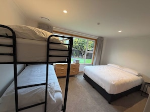A room with bunk beds, a window with curtains, a small wooden dresser, and a carpeted floor. - Hokowhitu Haven | Style, Space & Luxury (Palmerston North)