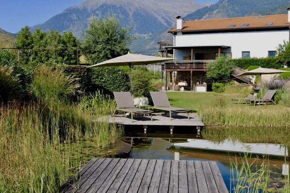 A wooden deck with lounge chairs and umbrellas overlooking a body of water, with mountains in the background. - Gapphof (Granny&Gala) (Algund)