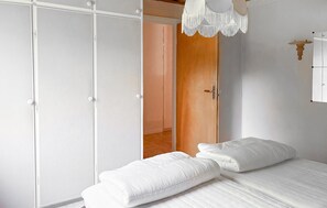 Un dormitorio con cama, ropa de cama blanca, un armario y una lámpara colgante.