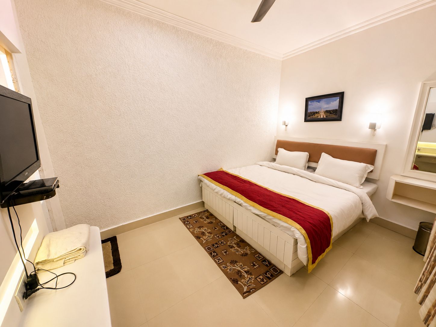 Une chambre d’hôtel comprenant un lit, une télévision, une table de chevet, une commode, une lampe fixée au mur et une fenêtre.