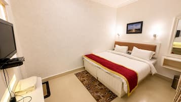 Une chambre d’hôtel comprenant un lit, une télévision, une table de chevet, une commode, une lampe fixée au mur et une fenêtre.