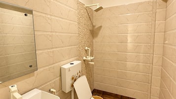 Casa de banho com parede revestida em mármore, chão de madeira, sanita branca e lavatório com bancada de mármore.