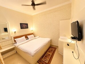 Une chambre d’hôtel équipée d’un lit, d’une table de chevet, d’une télévision et d’un ventilateur de plafond.