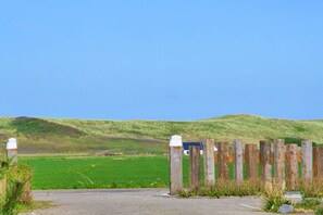 A rural landscape with a wooden fence, a paved road, and a grassy field. - Holiday home in Callantsoog with barbecue (Callantsoog)