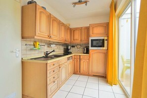A compact kitchen with wooden cabinets, a microwave, and a sink. - Holiday home in Callantsoog with barbecue (Callantsoog)