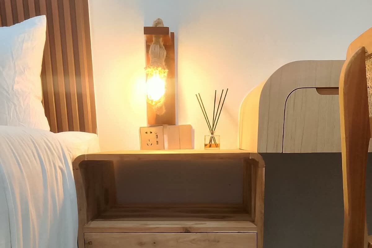 A bedroom with a wooden bedside table, a nightstand, a lamp, and a bed with white bedding.
