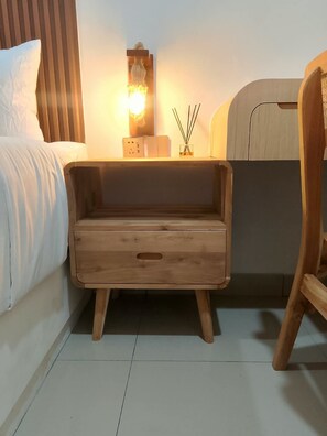 A bedroom with a wooden bedside table, a nightstand, a lamp, and a bed with white bedding.