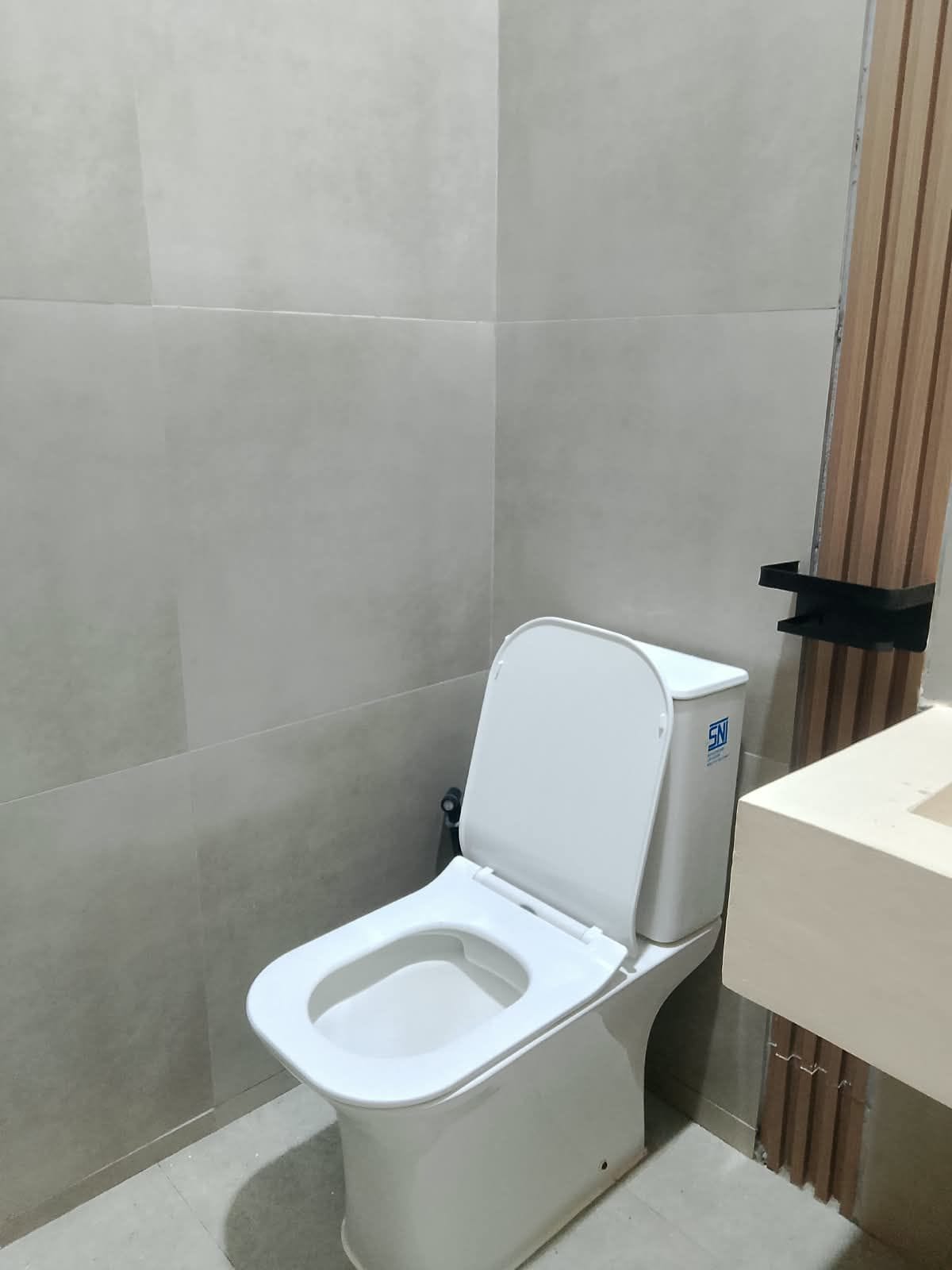 A modern toilet with a closed seat, a wall-mounted bidet, and a plain tiled wall.