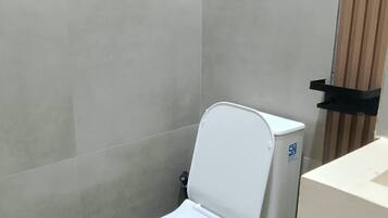 A modern toilet with a closed seat, a wall-mounted bidet, and a plain tiled wall.