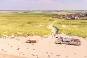 Een strand met een zandstrand, een pad naar een duingebied en een klein gebouw met een dak.