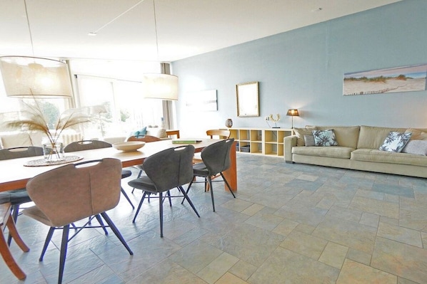 Een moderne woonkamer met een eethoek, met een bank, stoelen, een salontafel en een open haard.