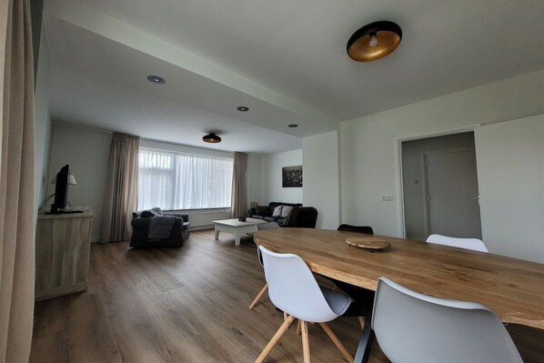 Un salon moderne avec une table à manger en bois, des chaises blanches, un canapé et un téléviseur.
