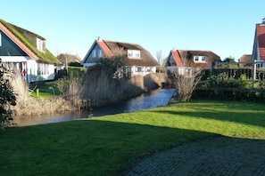 A residential area with houses, a narrow water channel, and a paved walkway. - Holiday home with 2 bedrooms (Callantsoog)