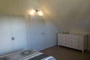 A bedroom with a sloped ceiling, a bed with a patterned bedspread, a dresser with drawers, and a white door. - Holiday home with 2 bedrooms (Callantsoog)