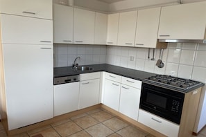 A kitchen with white cabinets, a stainless steel sink, a dishwasher, a stove, and a microwave. - Holiday home with 1 bedroom (Julianadorp)