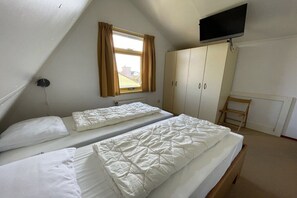 A room with two beds, a television mounted on the wall, a window with curtains, and a wardrobe. - Holiday home with 1 bedroom (Julianadorp)