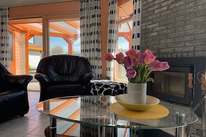 Een moderne woonkamer met een glazen salontafel, een open haard en uitzicht door grote ramen.