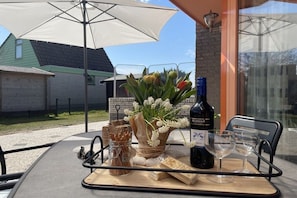 Een buitentafel gedekt, met een fles wijn, glazen, een pot koekjes en een bloemenboeket.