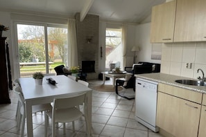 Une cuisine équipée d’un lave-vaisselle, une table à manger avec des chaises, une cheminée et une vue sur l’extérieur.
