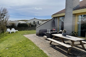 Un espace patio avec une table et des bancs en bois, un mur en briques grises et une clôture blanche.