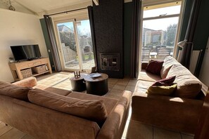 Een woonkamer met een bank, een televisietoestel, een open haard en een uitzicht door een glazen deur.