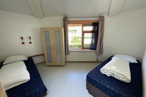 Een kamer met twee bedden, een kledingkast, een raam met gordijnen en een radiator.