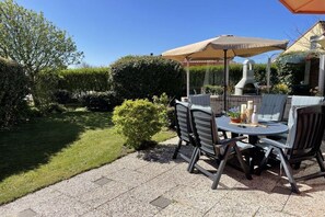 Een terras buiten met een ronde tafel, stoelen en een barbecue.