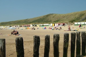 Een strand met houten palen op de voorgrond, een zandstrand en een rij kleurrijke strandhutten in de verte.