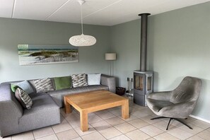 A living room with a sofa, a coffee table, a chair, a fireplace, and a hanging light fixture. - Holiday home Duynopgangh 27 (Julianadorp)