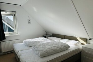 Een slaapkamer met twee bedden, een raam, een radiator en een nachtkastje met een lamp.