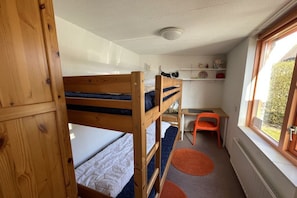 Een slaapkamer met stapelbed, bureau en stoel, een raam met uitzicht, en een plank met decoratieve spullen.