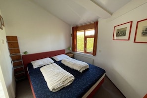 Een slaapkamer met een bed, een raam met gordijnen, een radiator en een wandplank.