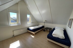 Un petit appartement d’une seule pièce, avec un plafond en pente, deux lits, un radiateur et une fenêtre.