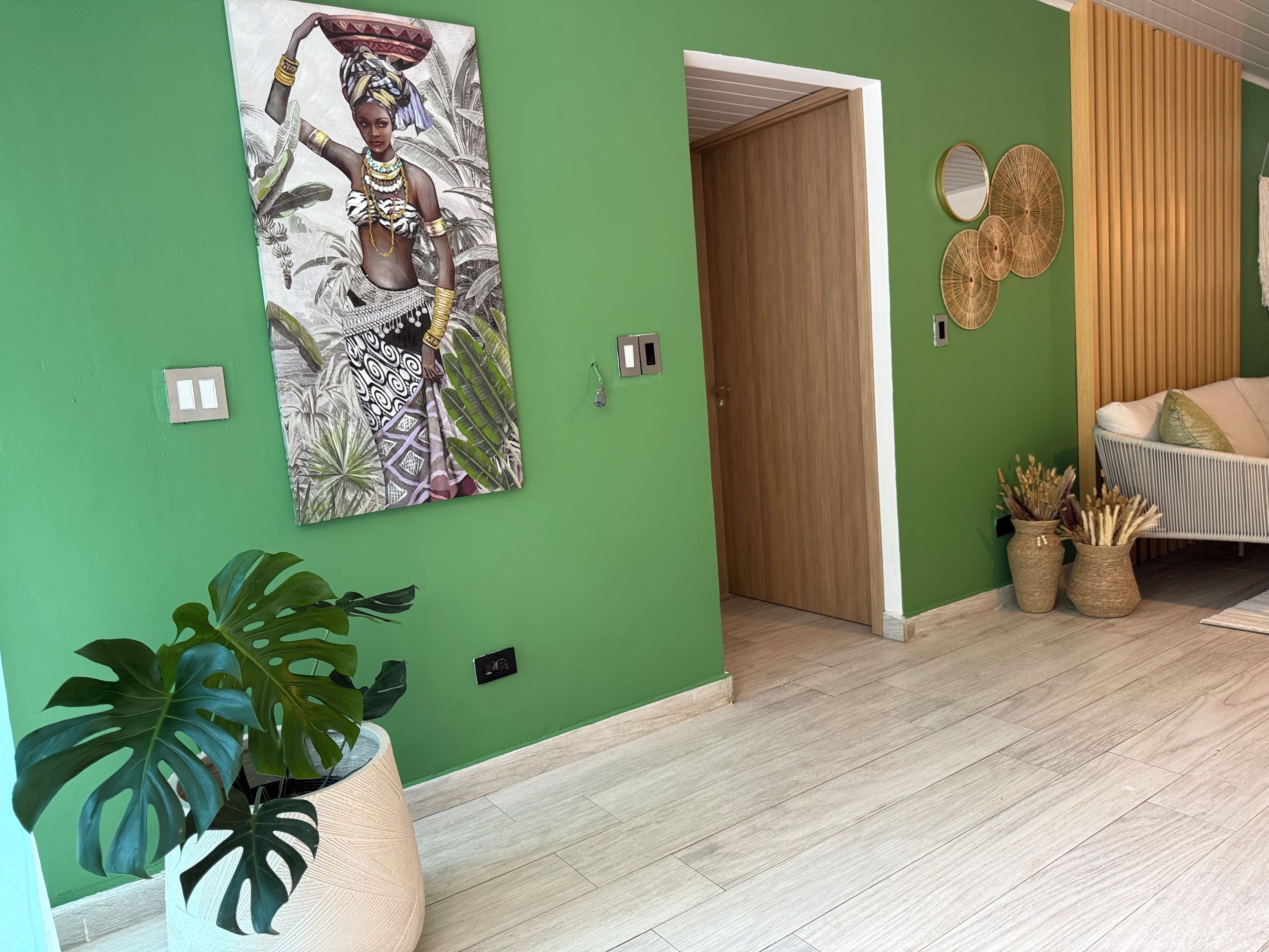 Une pièce avec un mur vert, une porte en bois, un canapé blanc avec des coussins et un grand tableau représentant une personne vêtue d’un costume traditionnel.