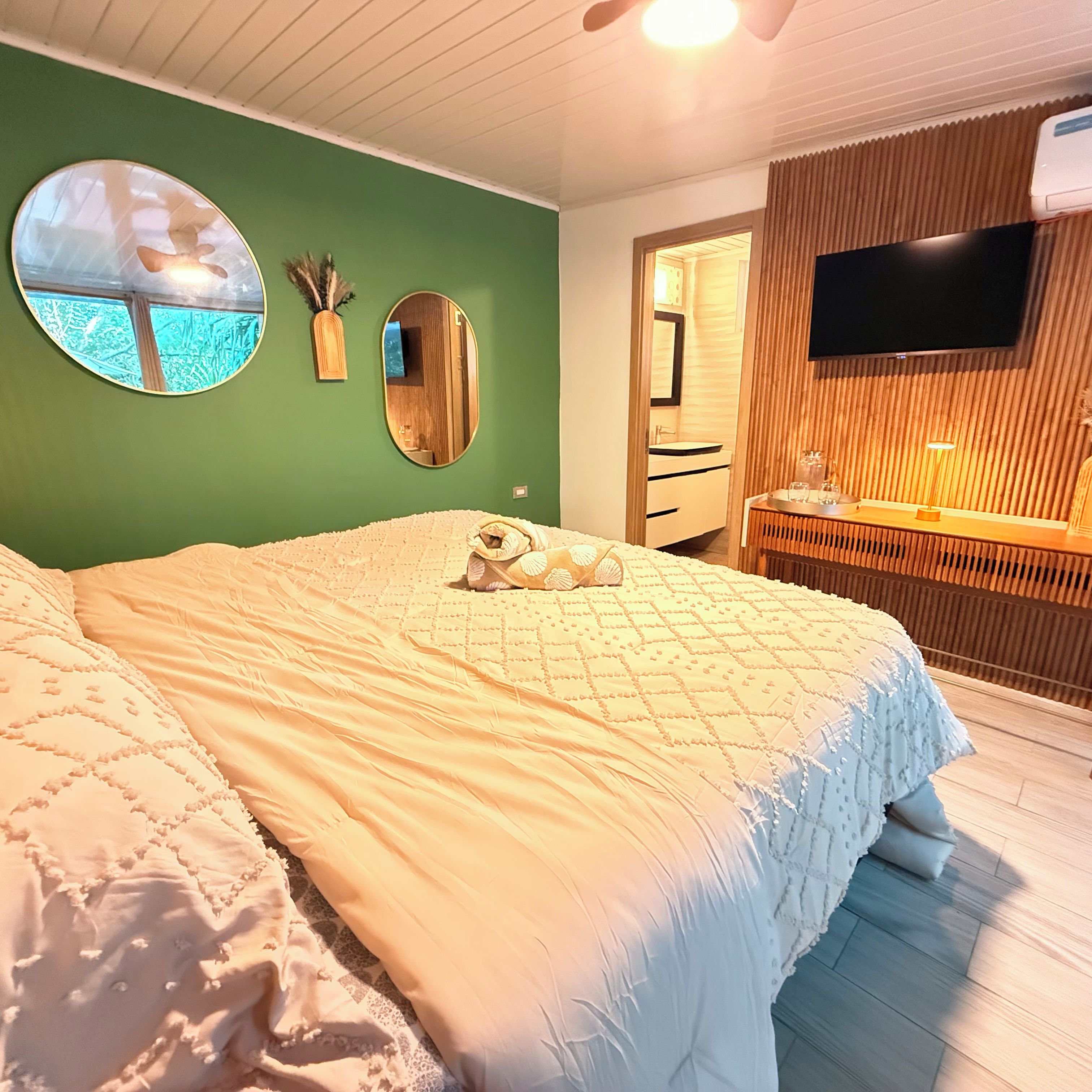 Une chambre à coucher avec un grand lit, un miroir rond, une coiffeuse en bois et un téléviseur à écran plat.
