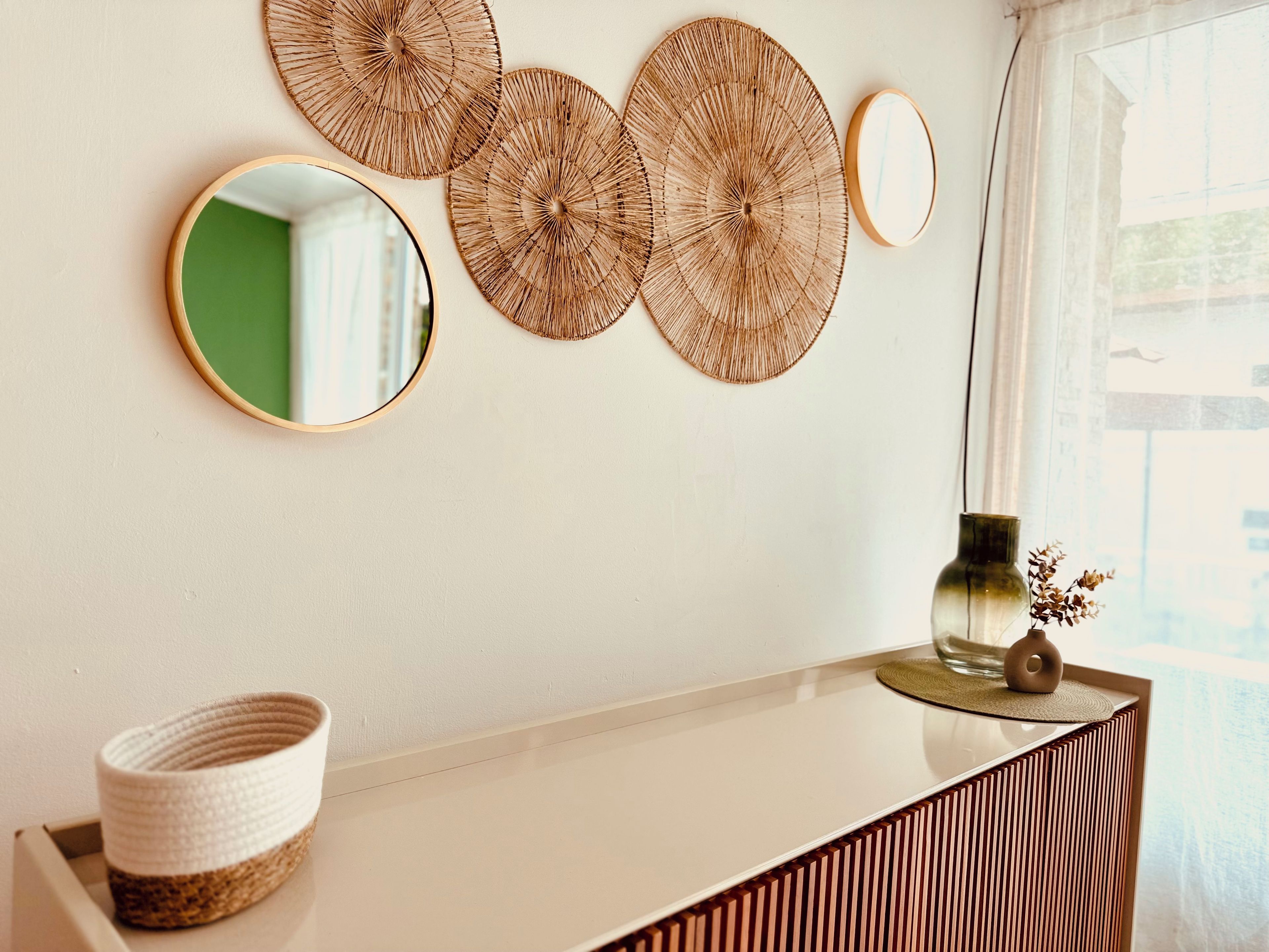 A wall with three circular wall decorations, a round mirror, and a vase with dried flowers on a white console table.