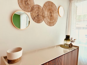 A wall with three circular wall decorations, a round mirror, and a vase with dried flowers on a white console table.