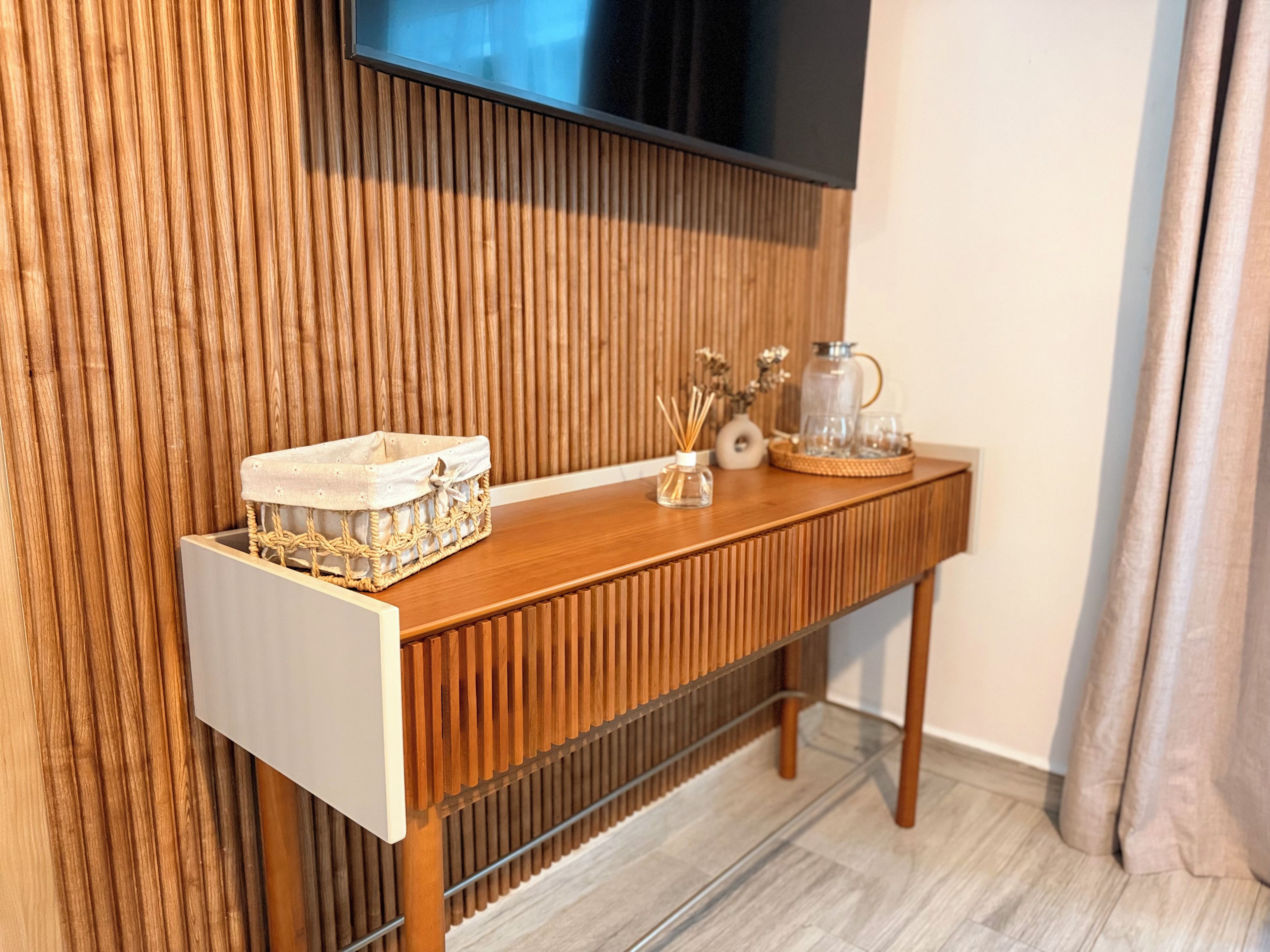 Une console en bois sur laquelle est fixée une télévision, un panier en osier et une carafe en verre posée sur la console.