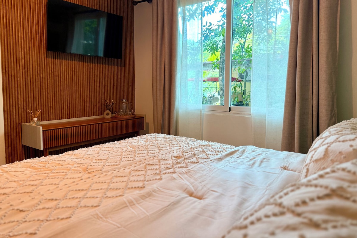 Un dormitorio con cama, televisor montado en la pared, ventana con cortinas y pared de paneles de madera.