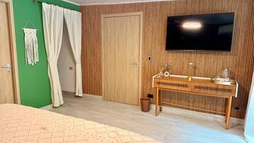 A room with a bed, a TV mounted on the wall, a wooden desk, and a green accent wall.